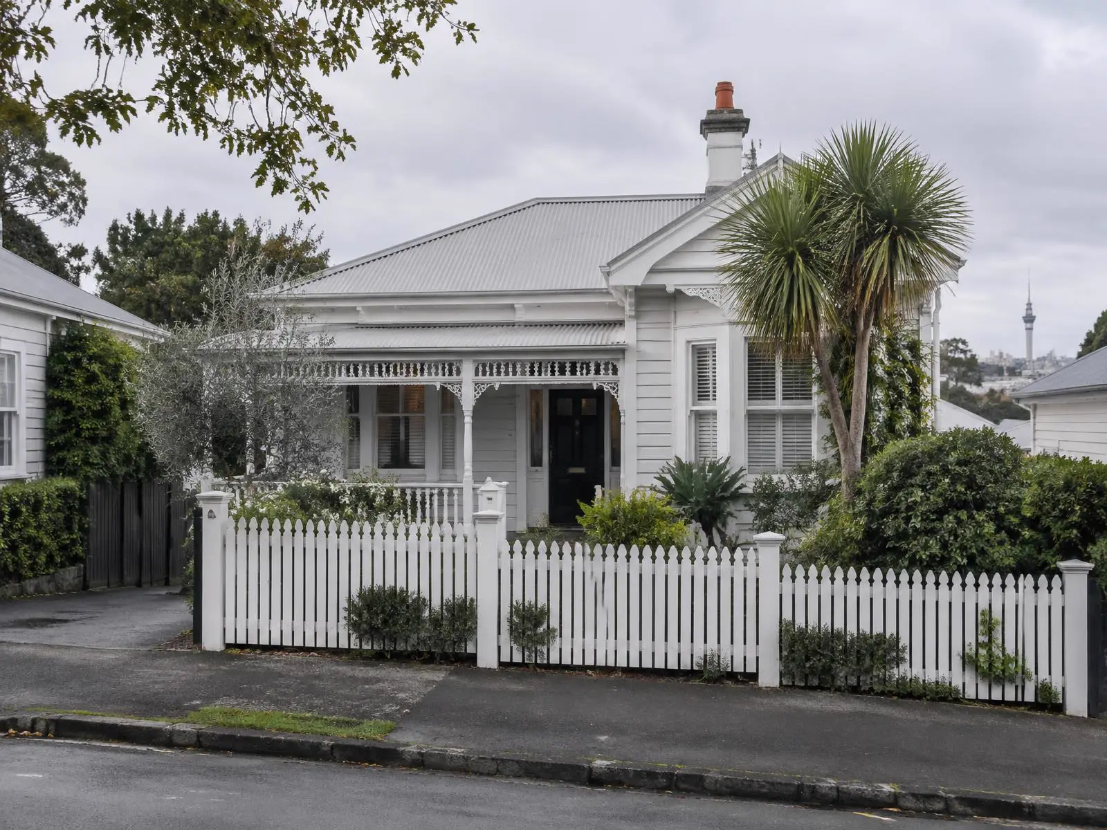 A white weatherboard villa behind a picket fence on a leafy Auckland street